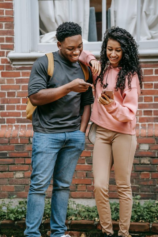 Two smiling young people watching something on phone.