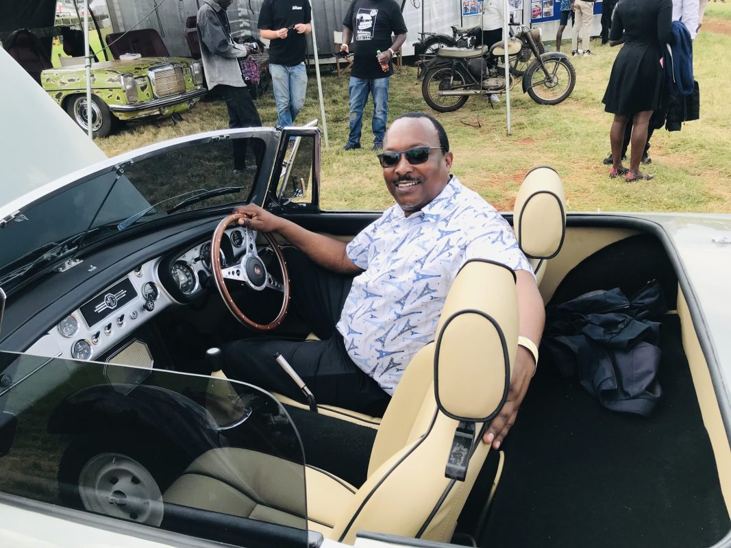 Photo of a smiling man at the wheel of an open car.